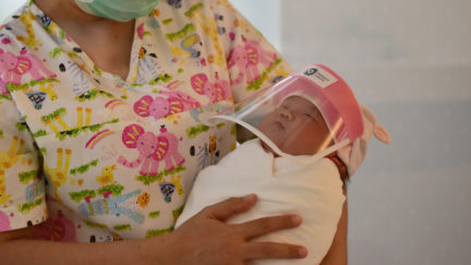 A nurse holding a newborn baby wearing a face shield, in an effort to halt the spread of the COVID-19 coronavirus