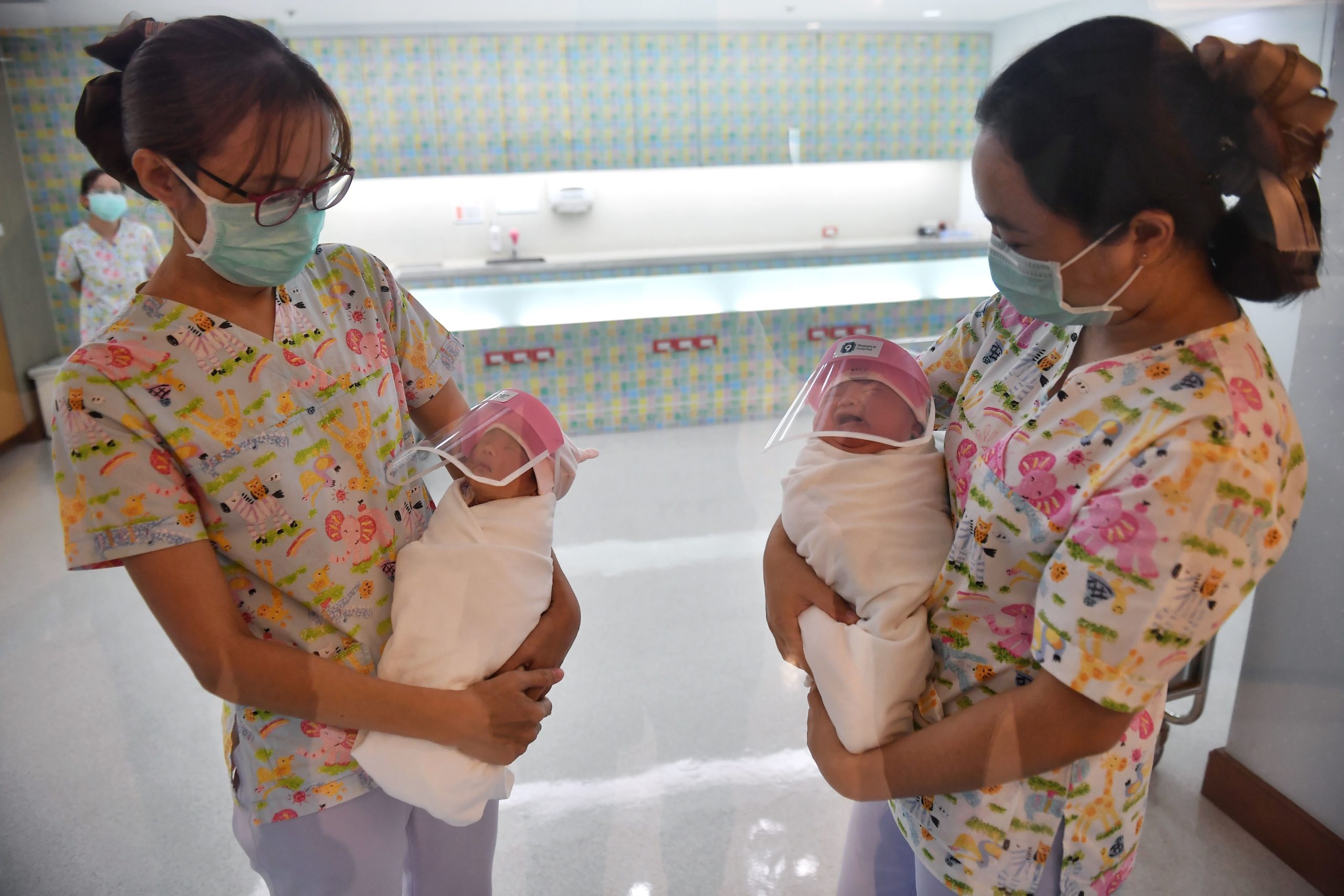 A nurse holding a newborn baby wearing a face shield, in an effort to halt the spread of the COVID-19 coronavirus