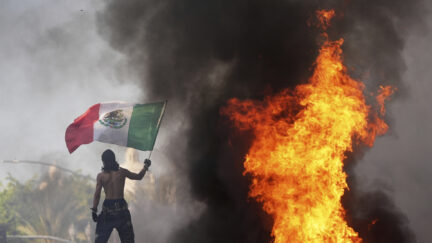A protester waves a flag as a Waymo taxi burns near the Metropolitan Detention Center of downtown Los Angeles, Sunday, June 8, 2025, following last night's immigration raid protest