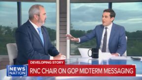 screenshot two men sitting in a tv studio with a mug on the table in front of them