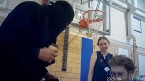 a person in a black burqa holding a coffee cup speaks to two people in a gym